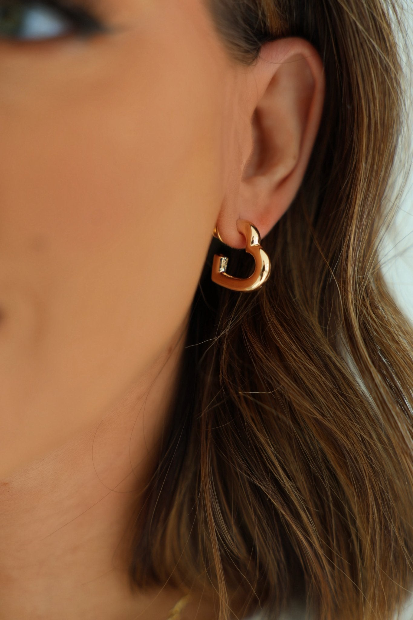 Close-up of a woman's ear in Gold Thick Heart Hoop Earrings, making a chic statement with her brown hair partially visible.