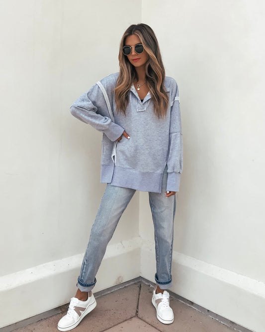 Woman in sunglasses wears a Grey Contrast Pullover Sweatshirt - FINAL SALE, light blue jeans, and white sneakers against a white wall.