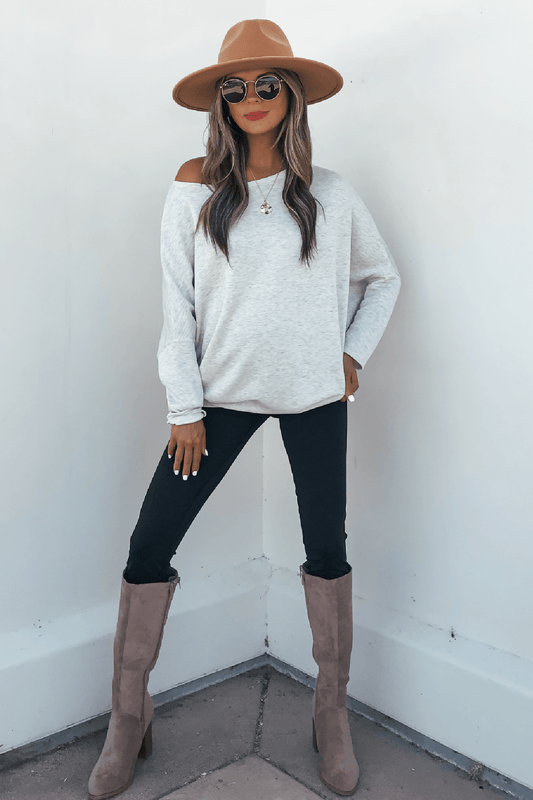 Woman in a hat, sunglasses, Grey Soft Cloud Scuba Pullover, black pants, and taupe boots stands against a white background.