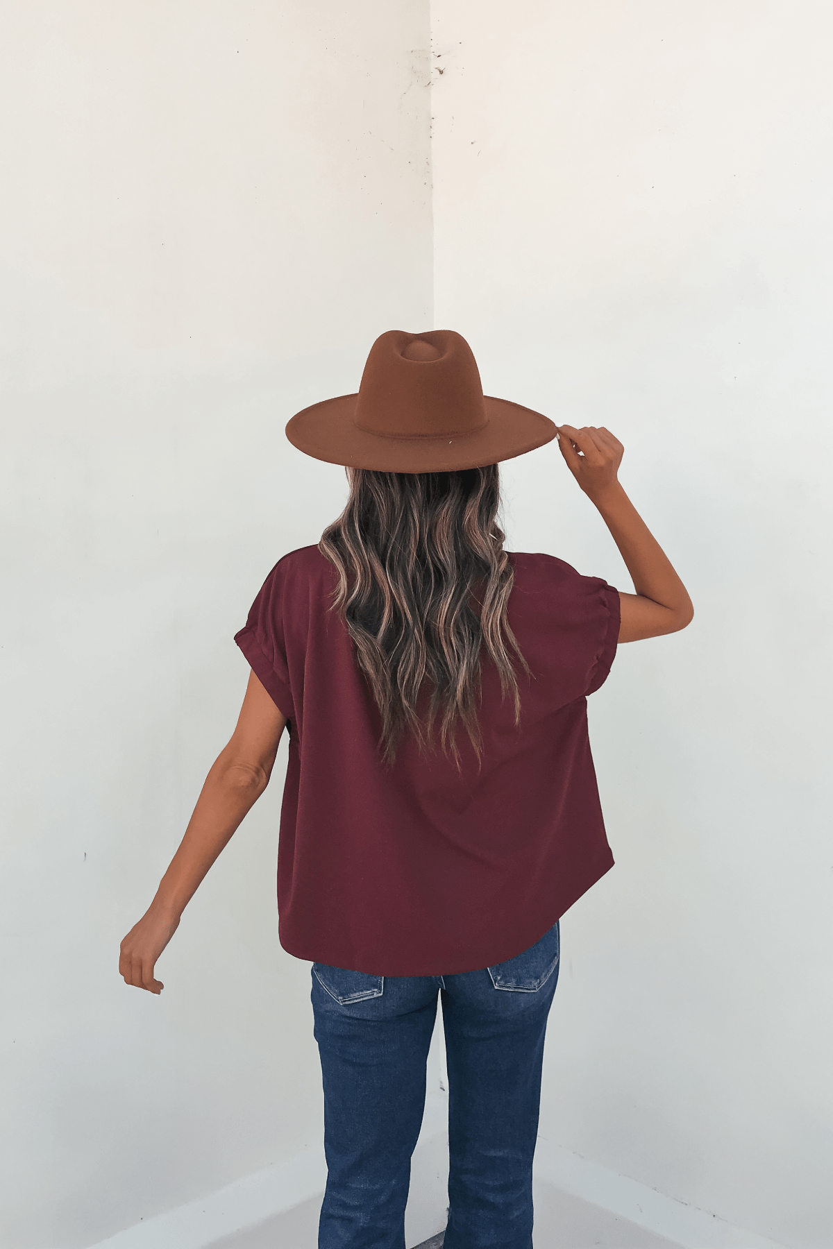 Wearing the Harlow Burgundy Short Sleeve Blouse with blue jeans and a brown hat, she creates an autumn-ready look.