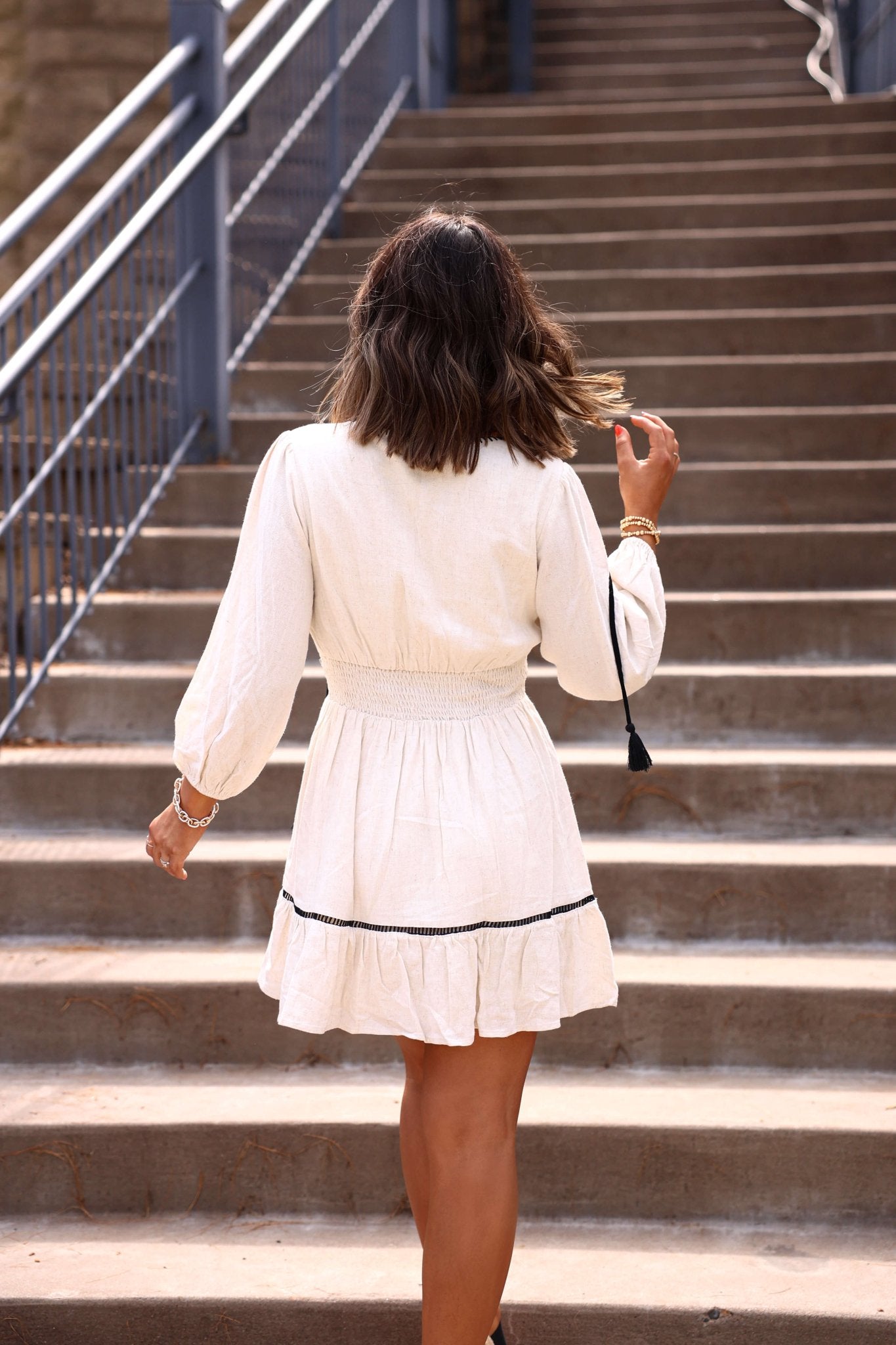 A woman in the Kylie Stitch Linen Mini Dress walks up outdoor stairs, her back to the camera.