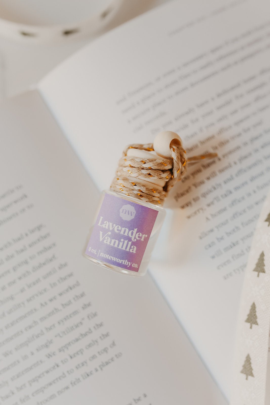 The Lavender Vanilla Car Diffuser - FINAL SALE is a perfect car air freshener or Christmas gift, shown with braided rope on an open book.
