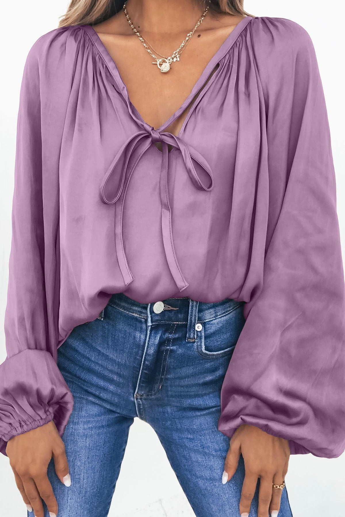 Woman wears Light Mauve Satin V Neck Blouse with blue jeans and layered gold necklaces.