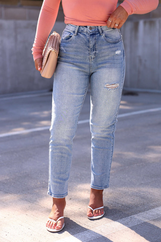 Woman in a peach top, Light Wash High Rise Cropped Straight Jeans (Final Sale), white sandals, and beige clutch outdoors.