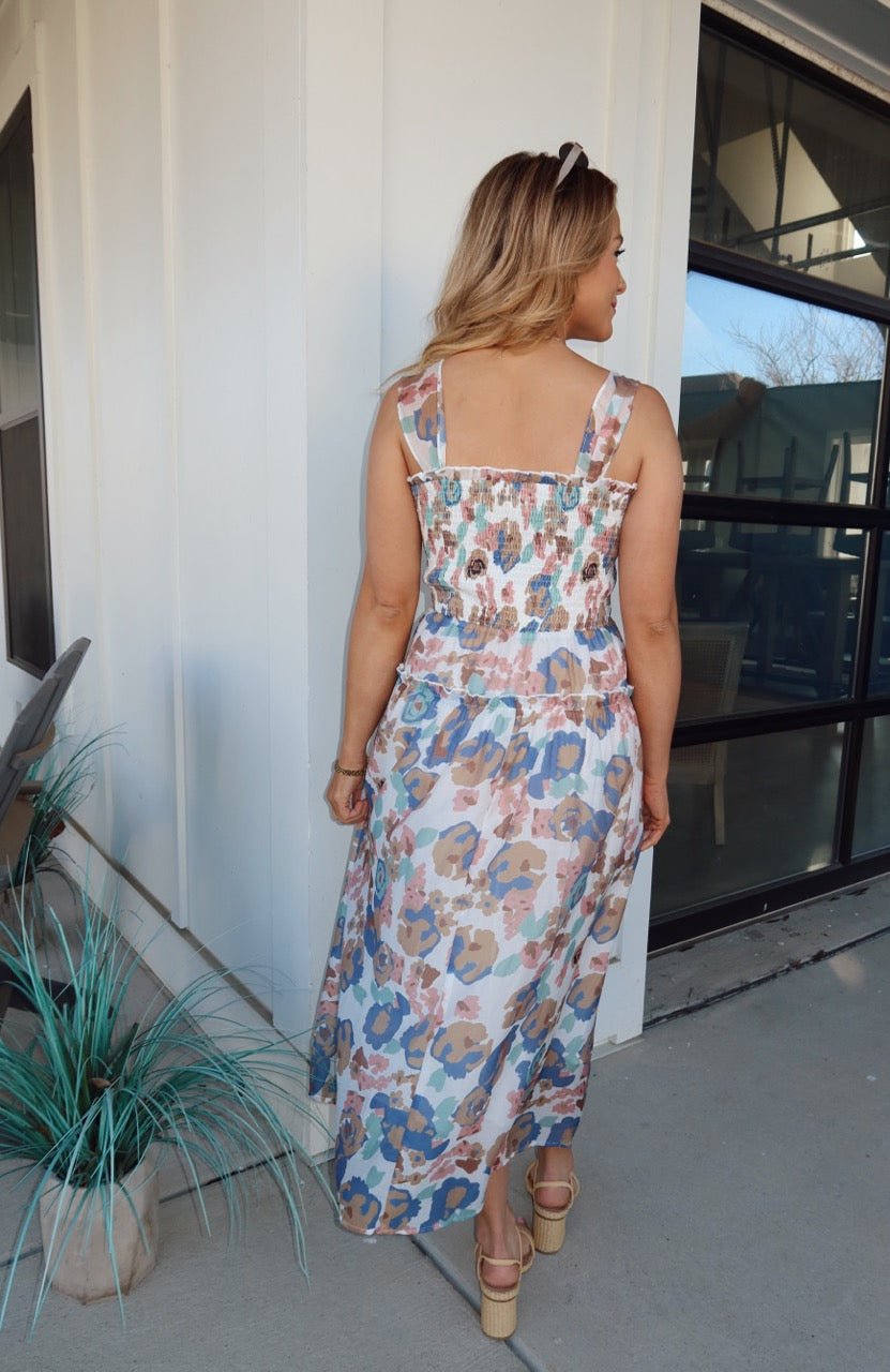 Woman on a patio wearing the Multi Floral Print Smocked Midi Dress, facing away from the camera near a large window.