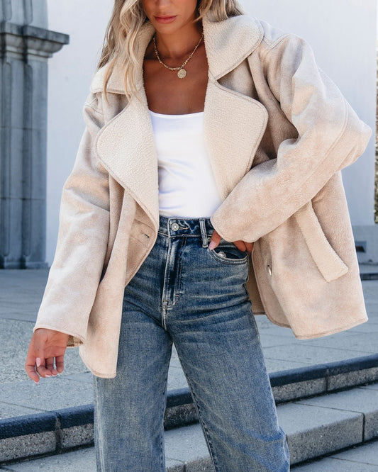 Woman in Muse By Magnolia Faux Suede Sherpa Jacket - Beige, white top & blue jeans, standing outdoors near stone steps.