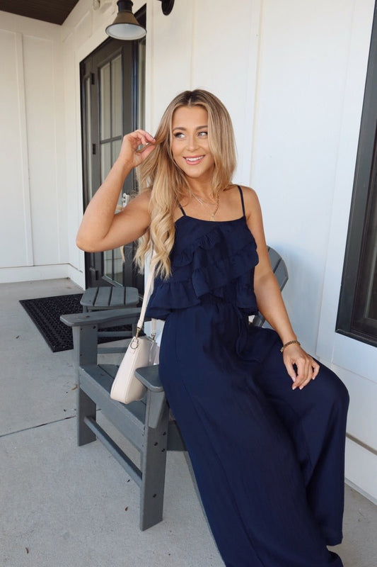 Woman with long blonde hair smiles, wearing the Navy Ruffled Cami Top and Pant Set - FINAL SALE on a gray outdoor chair.
