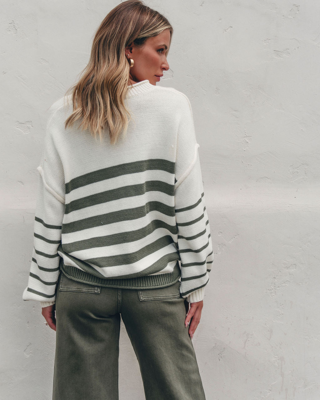 Woman with wavy blonde hair in the Olive and Cream Striped Pullover Sweater—FINAL SALE, styled with green pants for fall.