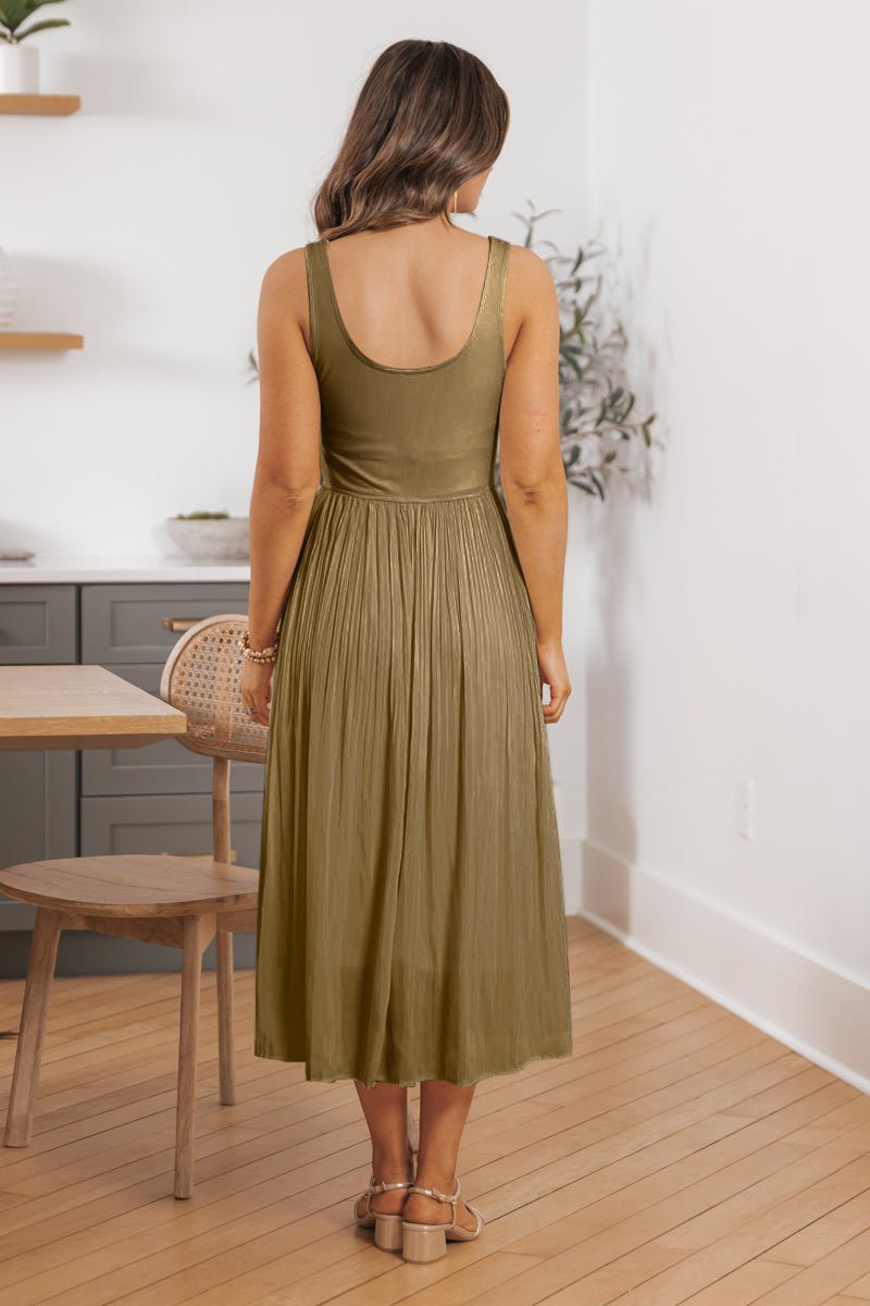 A woman stands indoors on a wooden floor, back to the camera, wearing the Olive Scoop Neck Pleated Tank Midi Dress - DOORBUSTER.