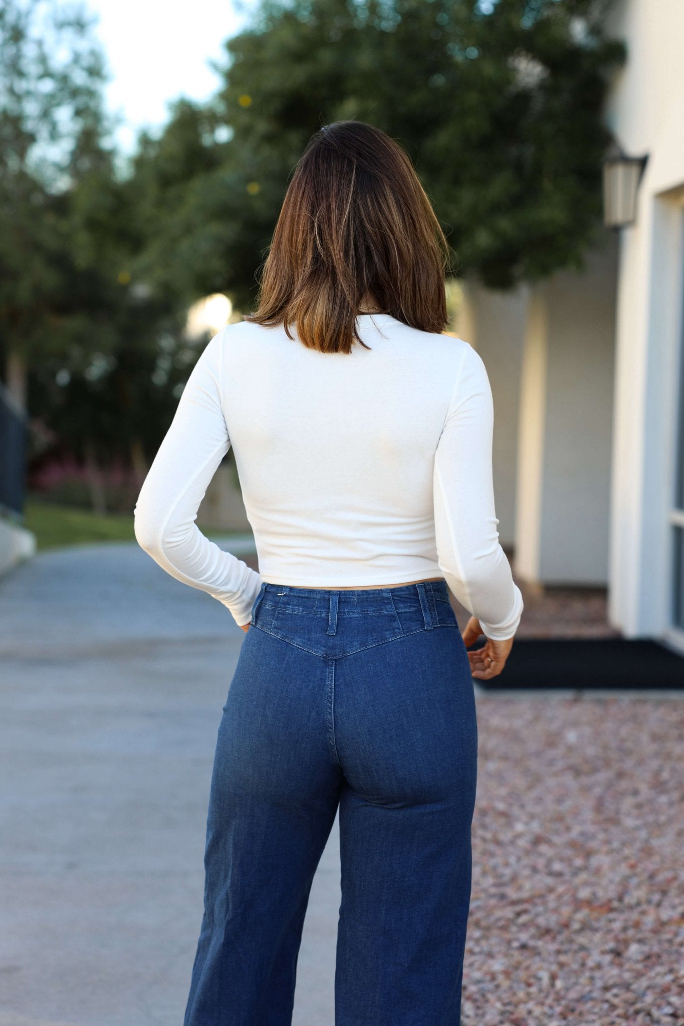 Wearing the Perfectly Smooth White Basic Top and relaxed-fit blue jeans, a woman stands outdoors facing away from the camera.