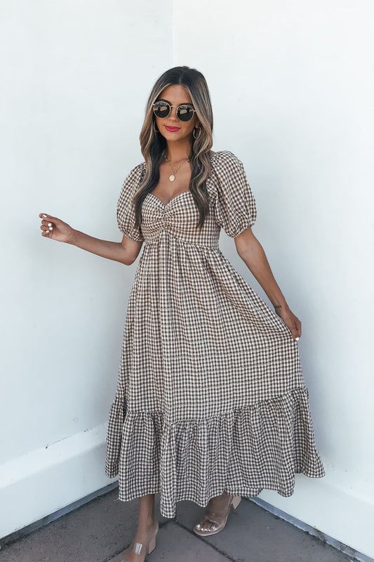 Woman in the Picnic Plaid Smock Midi Dress - Mocha with sunglasses and clear heels poses by a white wall.