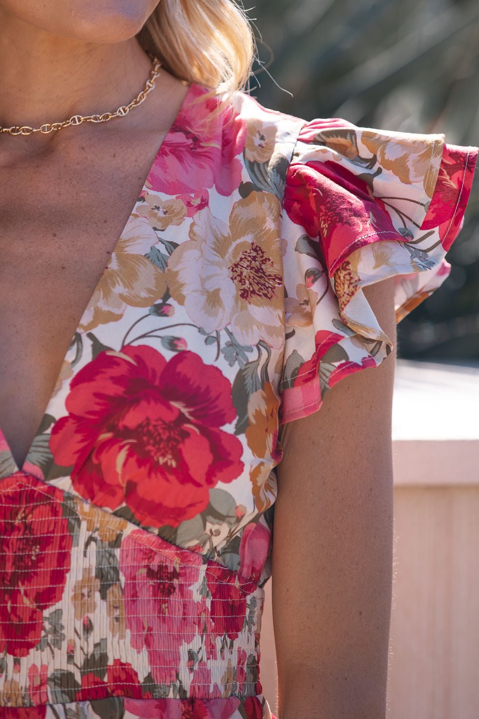 Close-up of a woman outdoors in sunlight, wearing a Pink Peony Print Ruffled Mini Dress and a gold chain necklace.