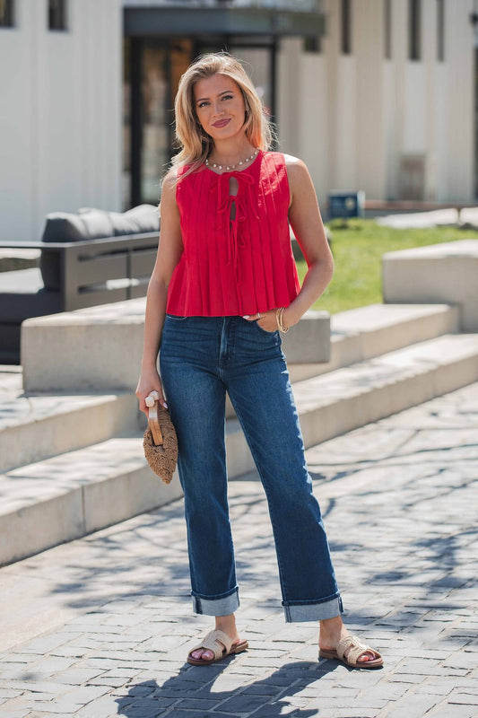 Woman wears Pleated Tie Front Top - Red, blue jeans, sandals, and holds a woven clutch outdoors on a sunny day.