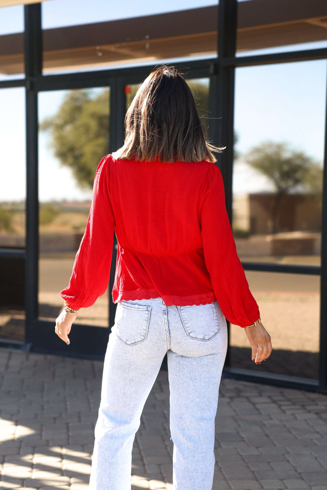 A woman in the Red Lace Trim Babydoll Top - FINAL SALE and light jeans stands outside, her fall style complemented by shoulder-length hair.