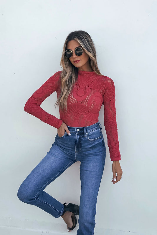 Woman in sunglasses wears the Red Mock Neck Fishnet Top - FINAL SALE with high-waisted blue jeans, posing against a white wall.