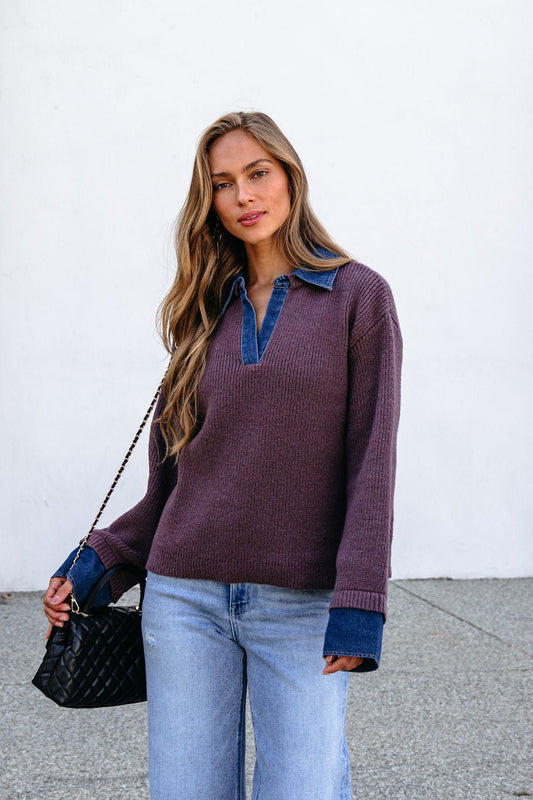 Woman with long hair in a Ribbed Denim Contrast Sweater - Mocha, light jeans, and a black purse stands against a white wall.