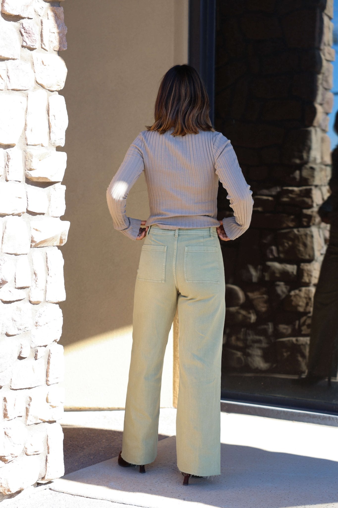 A woman stands outside with her back to the camera, wearing Sage Straight Wide Leg Pants and a beige top for a chic casual look.