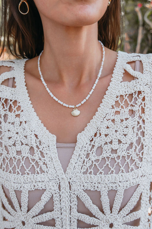 A woman wears the Seabreeze Pearl Shell Pendant Necklace and a cream crochet floral top over a beige tank.