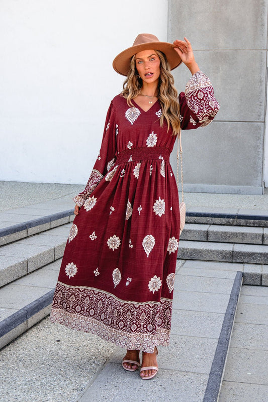 A woman wearing a Printed Long Sleeve Maxi Dress - Brown in a burgundy floral boho style with long sleeves and a wide-brimmed hat.