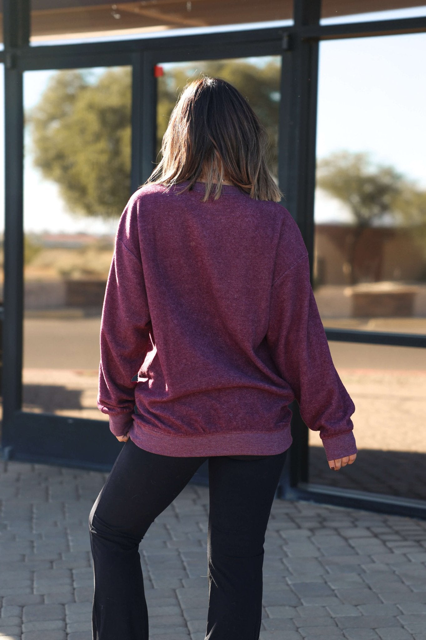 A woman with shoulder-length hair stands outside, wearing the Soft Brushed Oversized Sweatshirt - Plum and black pants.