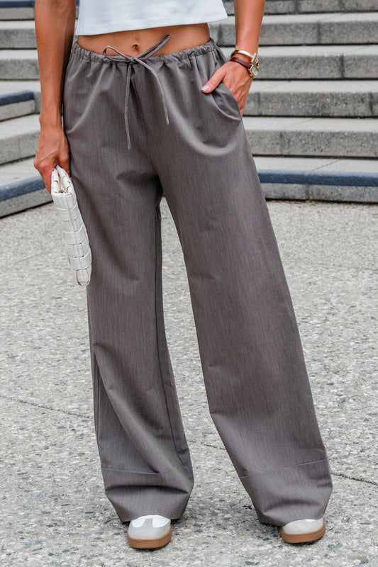 Person in brown Steve Madden Idra Pants, white crop top, and sneakers holds a clutch on a stone staircase.