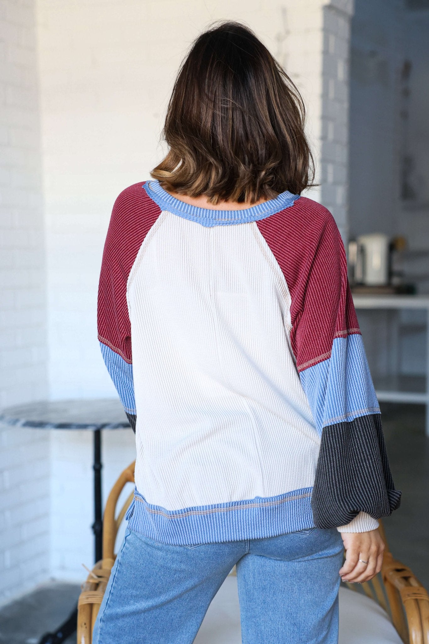 A woman with shoulder-length brown hair wears the Stone Multi Color Block Ribbed Pullover in a bright, modern room.