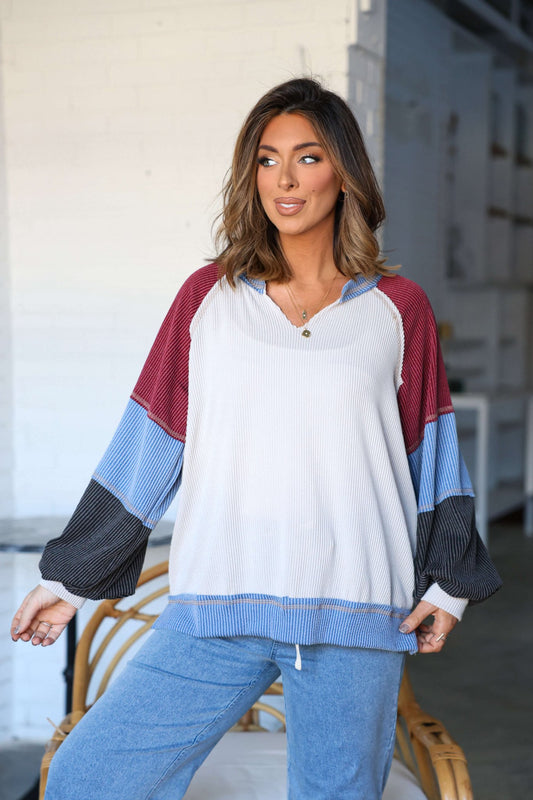 A woman models the Stone Multi Color Block Ribbed Pullover indoors, posing with one hand on a chair.