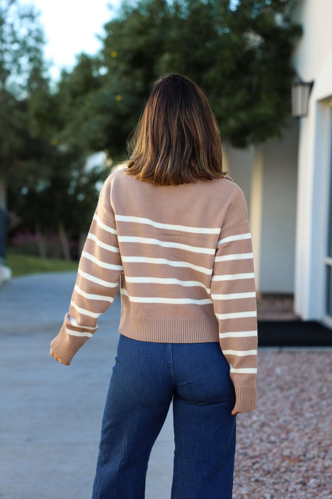 A woman with shoulder-length hair wears a Taupe and Cream Striped Quarter Zip Pullover, standing outdoors with her back to the camera.
