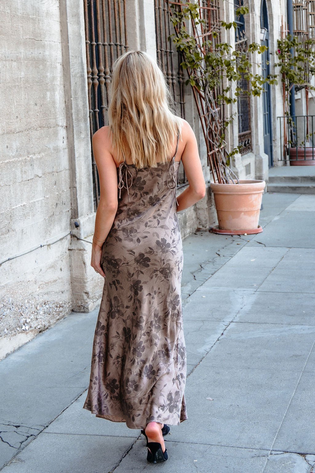 Woman with long blond hair walks on a sidewalk in a Taupe Floral Print Satin Slip Dress, facing away from the camera.