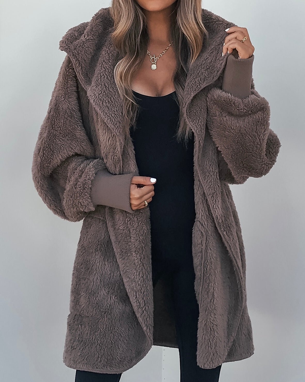 Woman in a long Teddy Fleece Hooded Cardigan, brown, over black with loose waves—collar held, the ultimate cozy winter look.