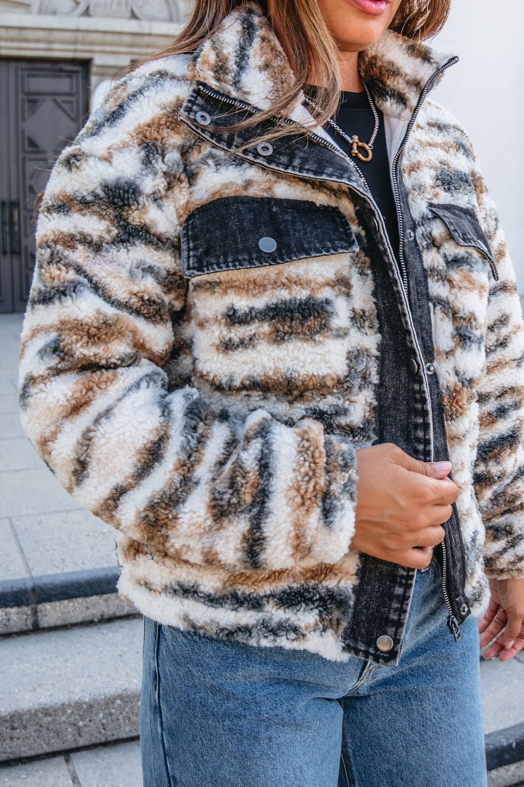 Woman wearing the Thread and Supply Cream Multi Print Sherpa Jacket - FINAL SALE, with black top and blue jeans, standing outside.
