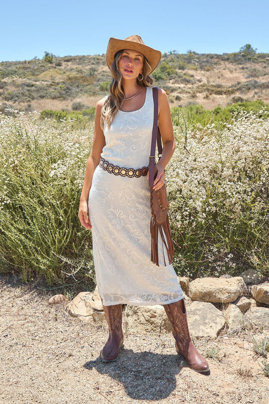 Woman in the Tucson Floral Lace Midi Dress - Ivory stands by wildflowers on a sunny day, wearing a cowboy hat and brown boots.