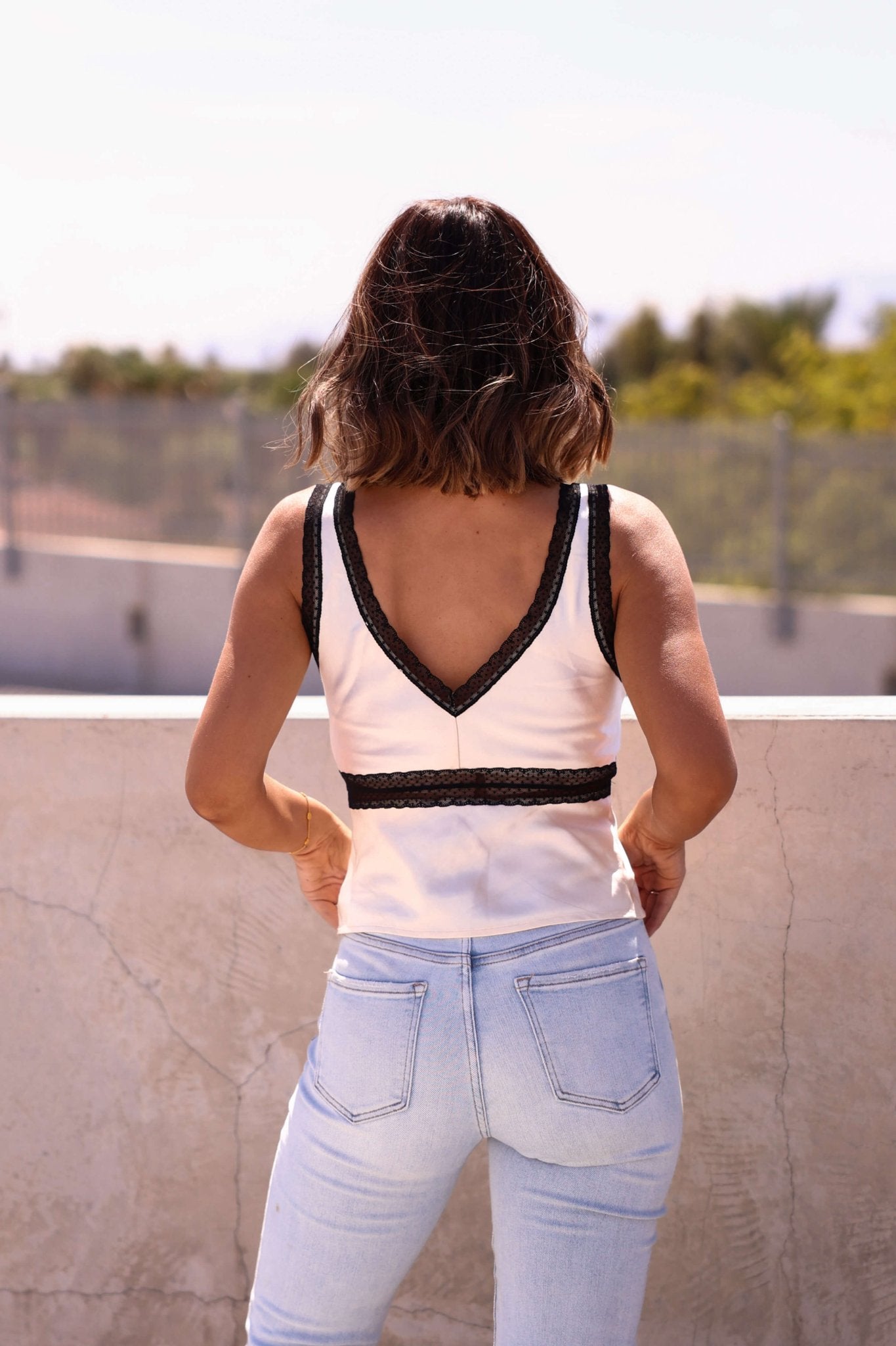 A woman wears the Vienna Black Lace Trim Satin Tank Top—an ideal choice for your fall wardrobe.