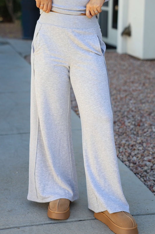 Person wearing Vintage Havana Heather Grey Ribbed Flare Pants and tan shoes, standing on a sidewalk next to gravel landscaping.