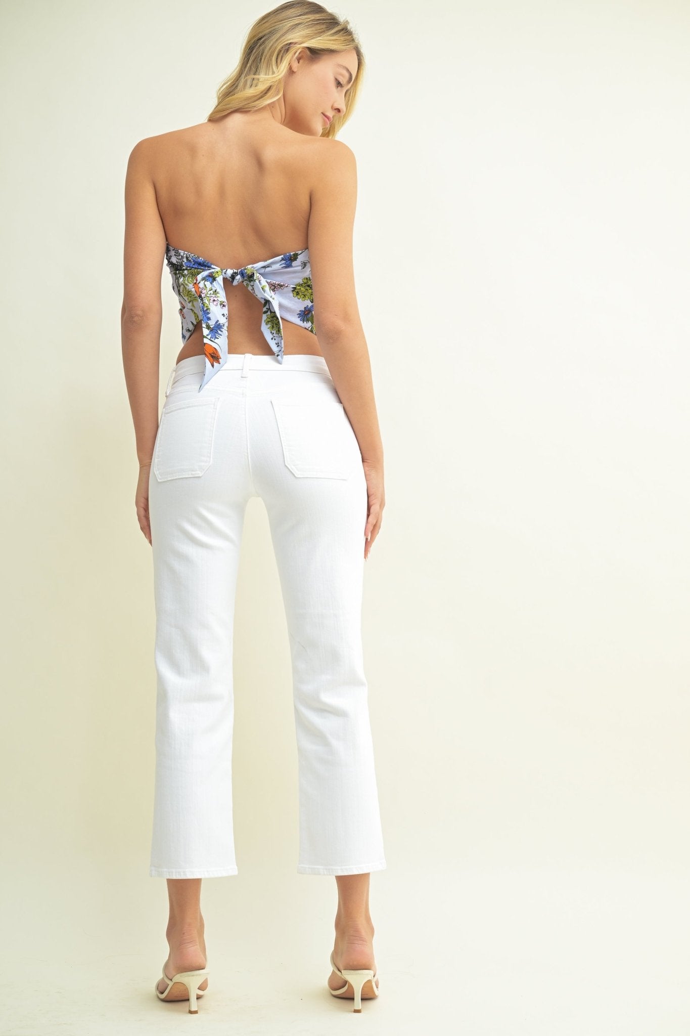 Woman wearing White Low Rise Straight Leg Jeans - FINAL SALE, heeled sandals, and a floral scarf top tied at the back.