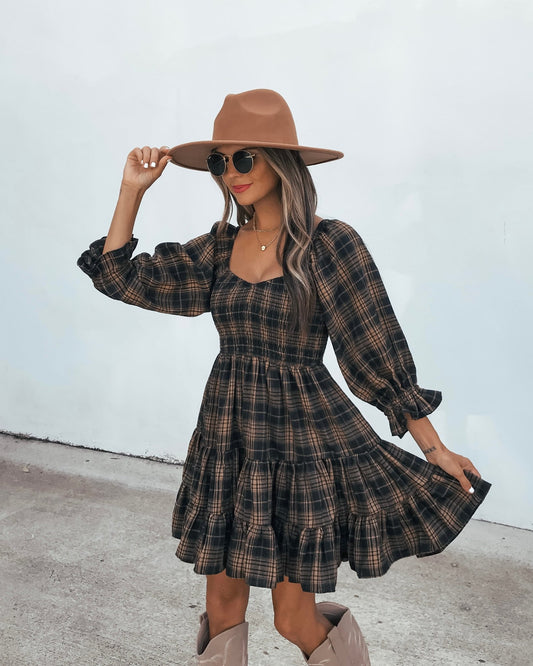 A person wears a black and tan Plaid Mini Dress - Black And Tan with long sleeves, a wide-brimmed hat, and tall boots.