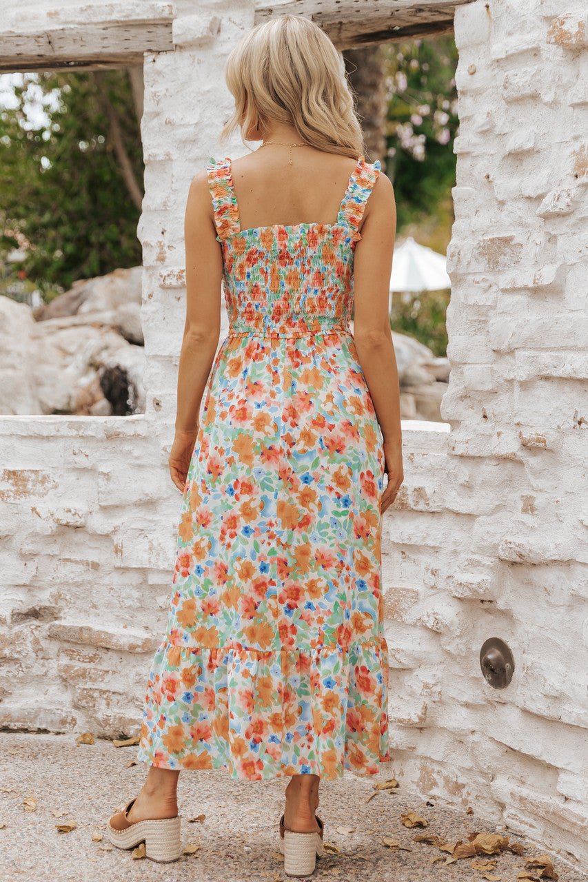 Woman in Caribbean Green Floral Smocked Maxi Dress faces a white stone wall outdoors, showing back and ruffle straps.
