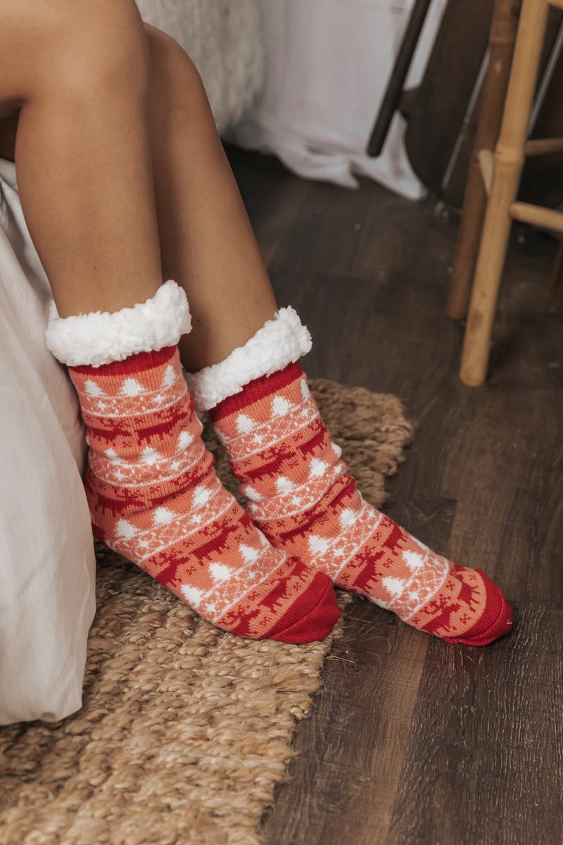 Someone wearing Fuzzy Fleece Red Nordic Christmas Socks sits on a woven rug by the bed.