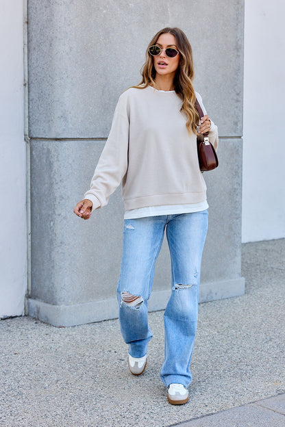 Woman in The Everyday Pullover - Clay, ripped jeans, and sneakers carries a brown bag for an effortlessly chic everyday look.