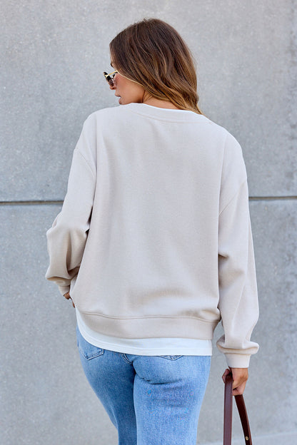 Woman wearing The Everyday Pullover - Clay and blue jeans stands with her back to the camera, holding a brown bag against a gray backdrop.