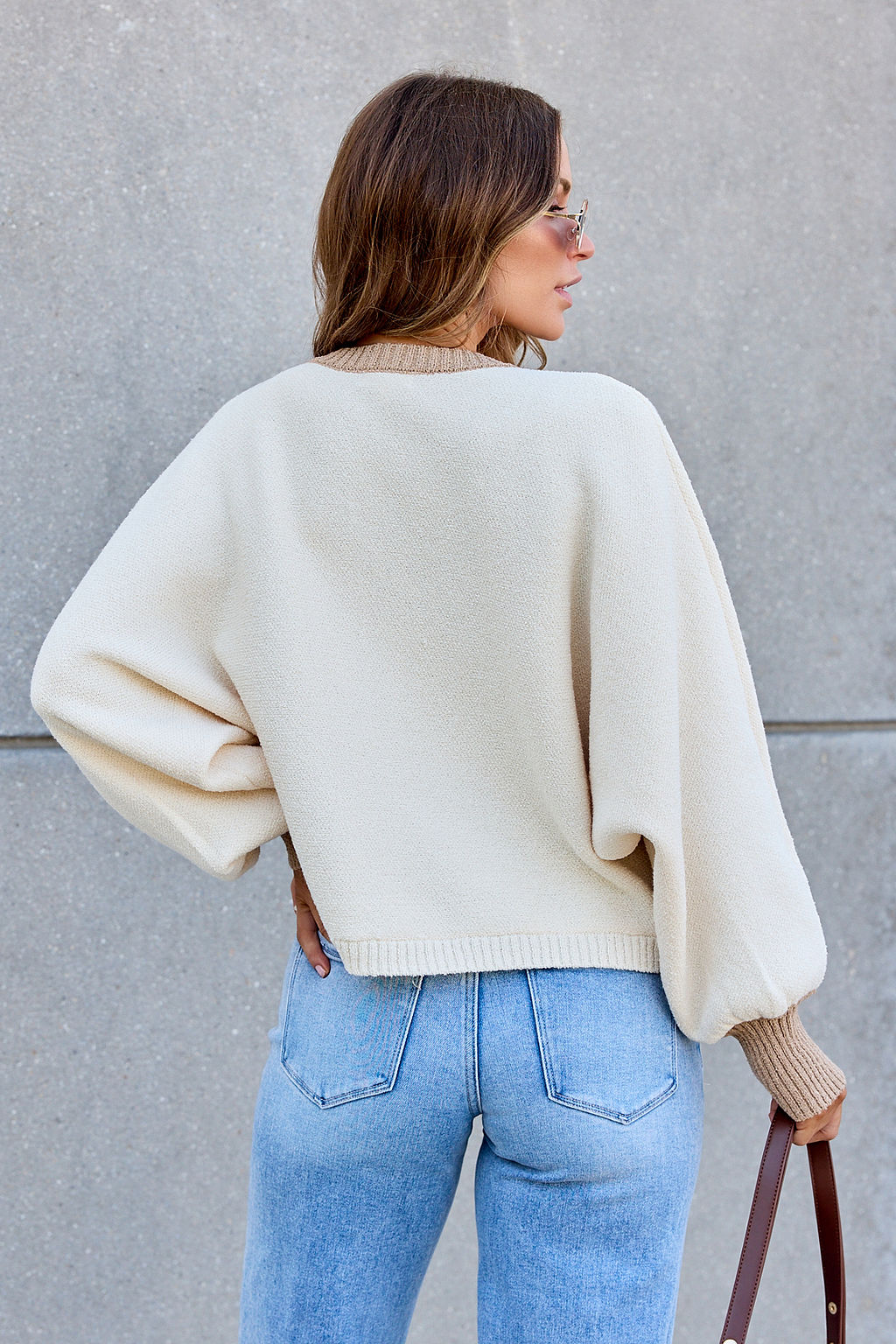 Woman with wavy hair in sunglasses wears the Contrast Ribbed Cardigan - Cream and light blue jeans, back to camera.