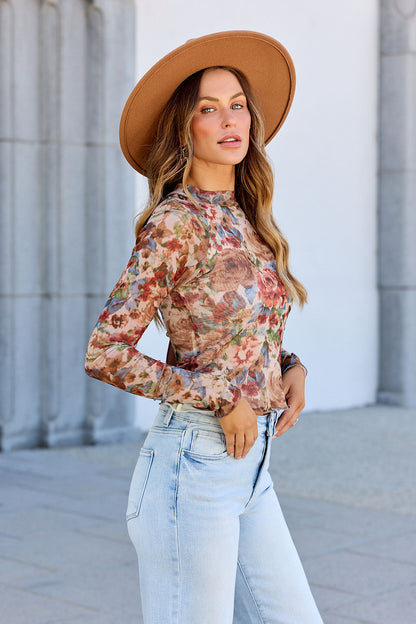 Woman in a brown hat, Elevated Floral Mesh Top - Cream, and light blue jeans stands outdoors by a building, looking at the camera.