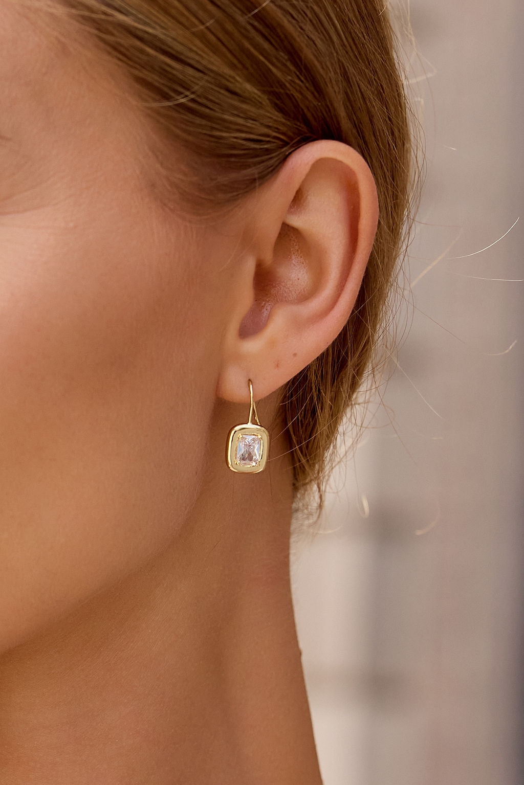 Close-up of an ear wearing Emerald Cut Drop Earrings - Gold, featuring a geometric silhouette with emerald cut cubic zirconia accents.
