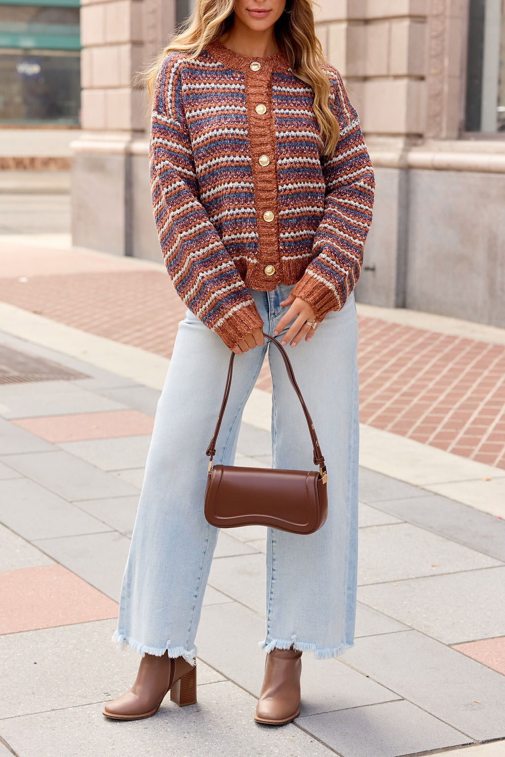 Woman in a Multi Striped Button Down Sweater, wide-leg jeans, brown boots, and handbag walking on a city sidewalk.