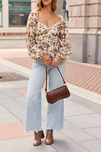 Woman in a Hazel Floral Print Top - Cream, light blue frayed jeans, brown boots, and handbag on a city sidewalk.