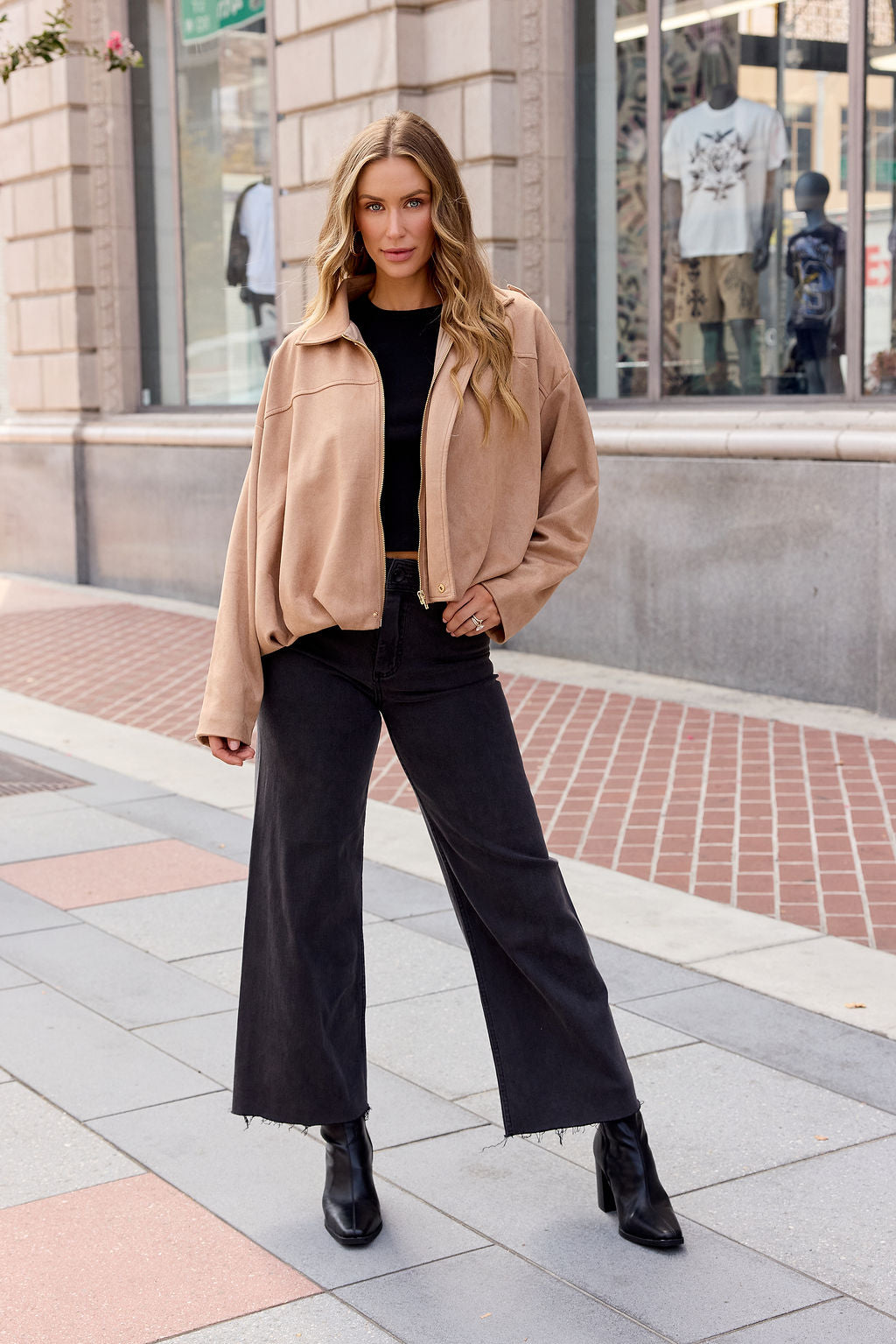 Woman in a Suede Bubble Hem Jacket - Camel, black top, wide-leg jeans, and boots poses stylishly on a city sidewalk—chic fall layering.