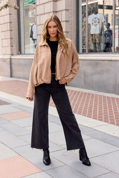 Woman in a Suede Bubble Hem Jacket - Camel, black top, wide-leg jeans, and boots poses stylishly on a city sidewalk—chic fall layering.