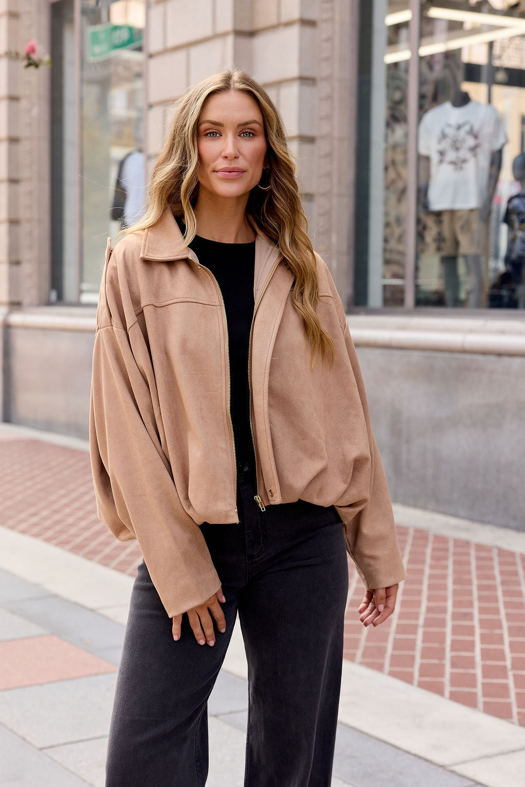Woman smiles on a city sidewalk in the Suede Bubble Hem Jacket - Camel and black pants—perfect for chic fall layering.