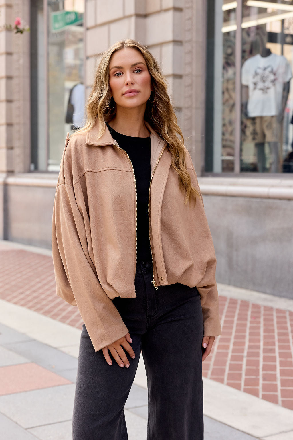 Woman in Suede Bubble Hem Jacket - Camel and black pants showcases chic fall layering on a city sidewalk, buildings behind her.