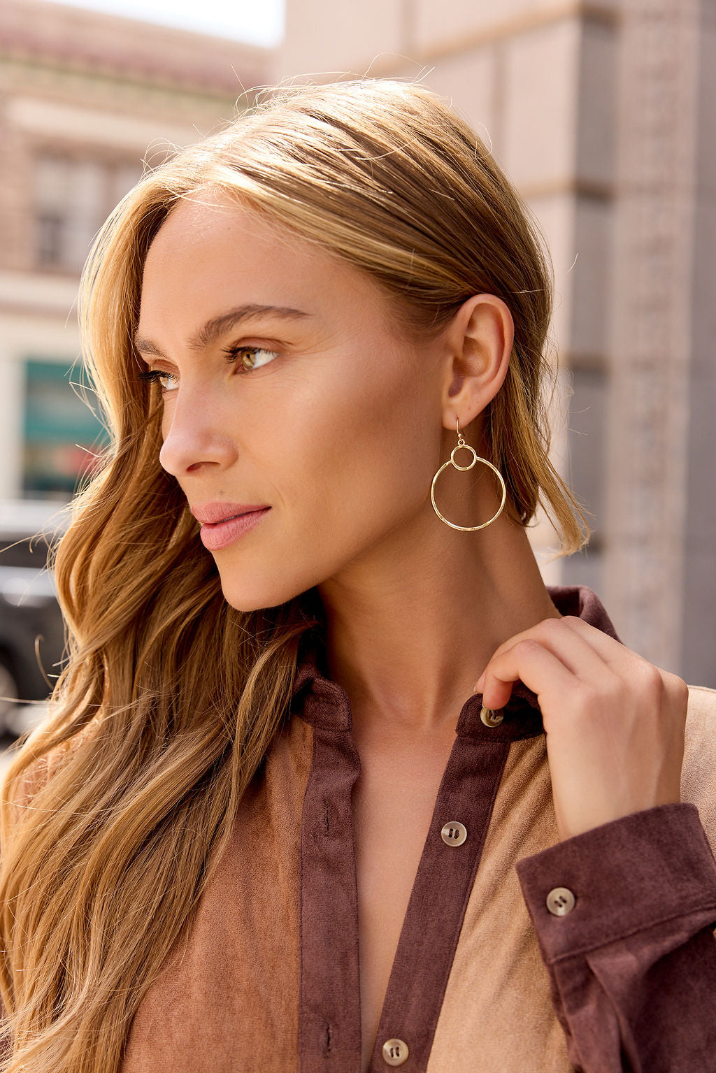 Woman with long blonde hair wears Halo Double Hoop Earrings in gold and a color-block shirt, looking to the side outdoors.